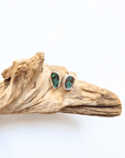 A pair of silver stud earrings with green opal inlays, displayed on a piece of natural driftwood against a plain white background.