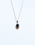 A silver chain necklace with a teardrop-shaped pendant featuring a dark blue oval gemstone surrounded by small clear stones, displayed on a plain white background.