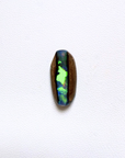 A polished oval cabochon gemstone showing vibrant iridescent play-of-color with green, blue, and purple hues, set in a natural brown opal matrix, displayed on a clean white textured background.