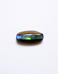 A polished oval cabochon pipe opal featuring a natural brown outer layer and a vibrant iridescent blue, green, and purple opal inlay, displayed on a textured white background.