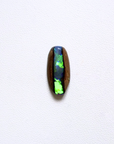 A polished oval cabochon gemstone featuring a vibrant green and blue opal inlay set on a dark brown wooden backing, displayed against a clean white textured background.